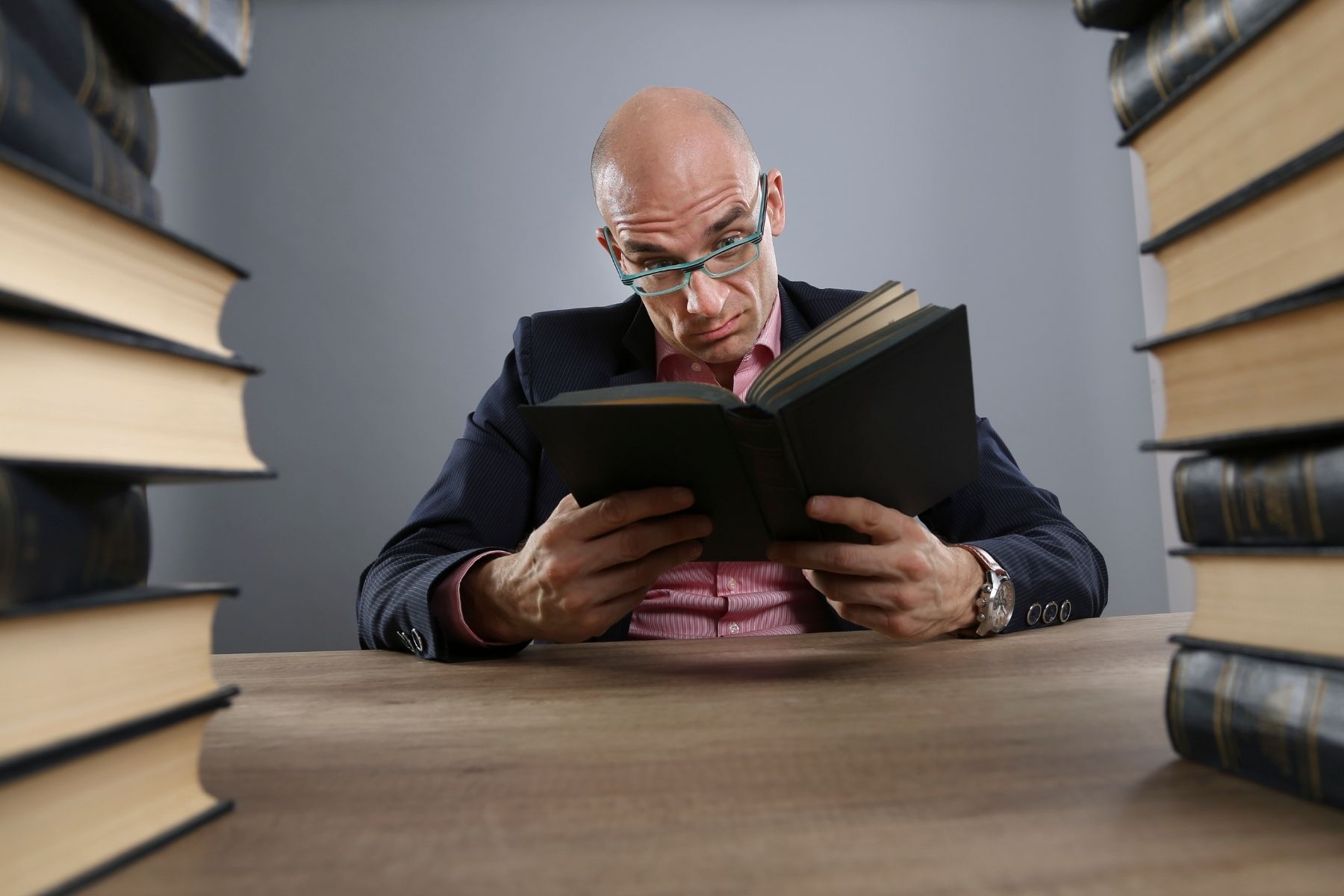 A white man surrounded by books looking frustrated
