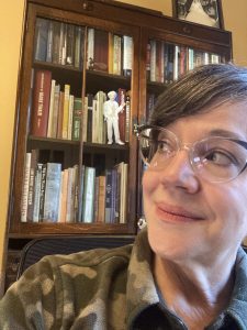 E.E. Burke glancing over her shoulder at a figurine of Mark Twain on her bookshelf