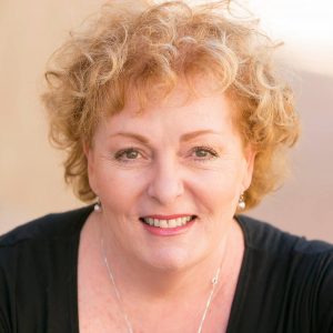 Besty Fasbinder is a white woman with curly blonde hair wearing a black blouse and beautiful silver necklace