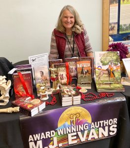 Image of Award Winning Author MJ Evans standing behind a table full of her books