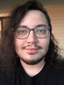 Scott is a white man with long dark brown hair and glasses