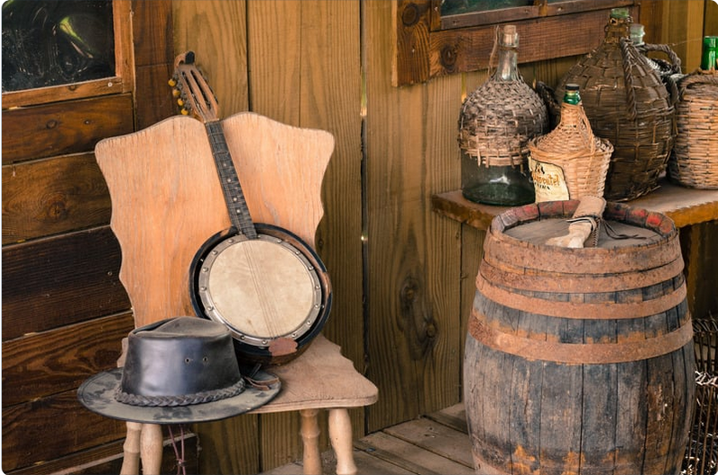 western themed porch with a barrel, bottles, and a hat and banjo on a chair