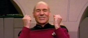 A bald white man in a red and black space exploration uniform celebrates