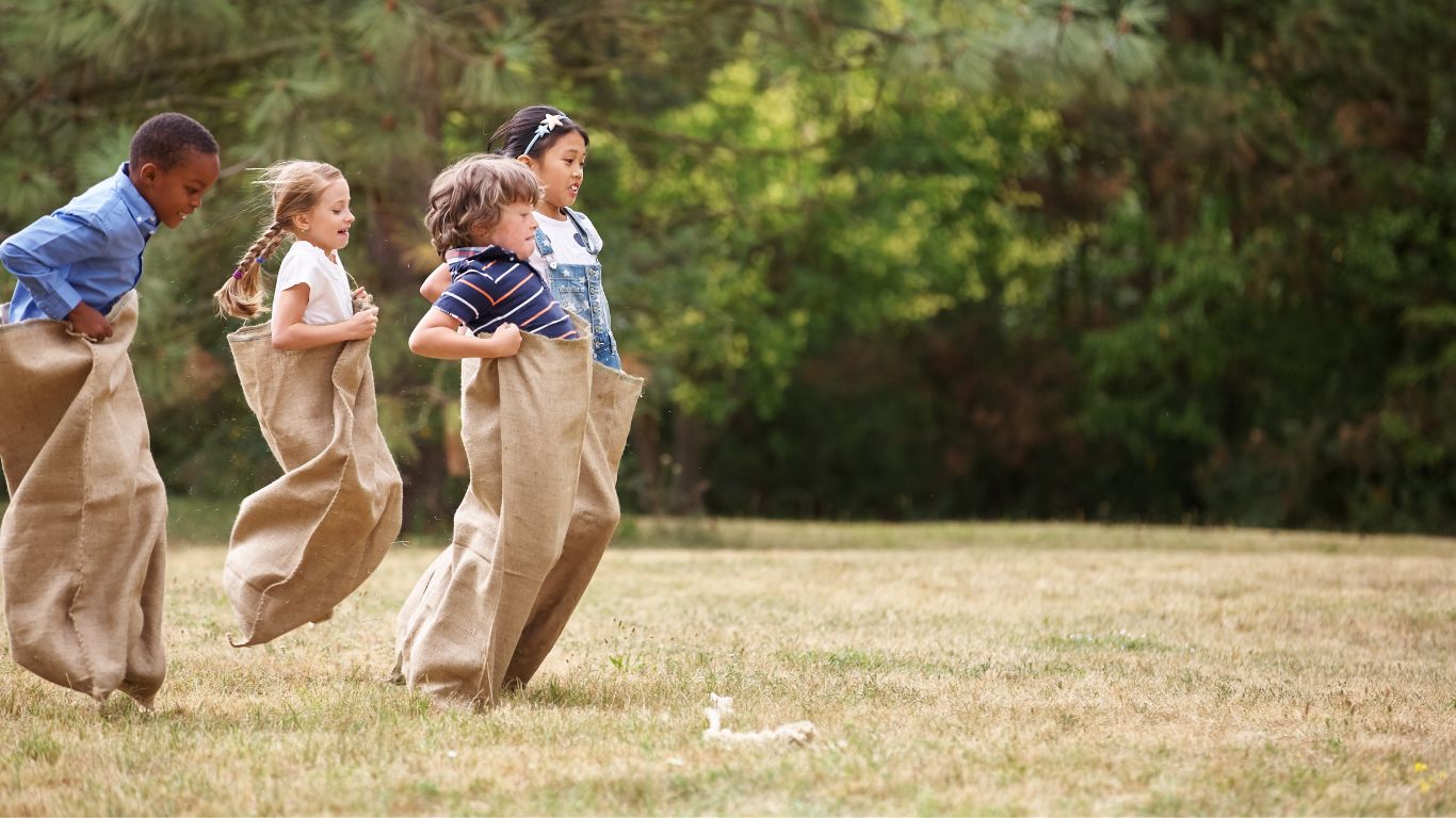 Sack races, grass, trees, kids, blue shirts, canvas bags