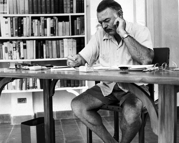 Hemingway, Library, books, writing, desk, chair, shorts, white shirt, glasses, writing, papers
