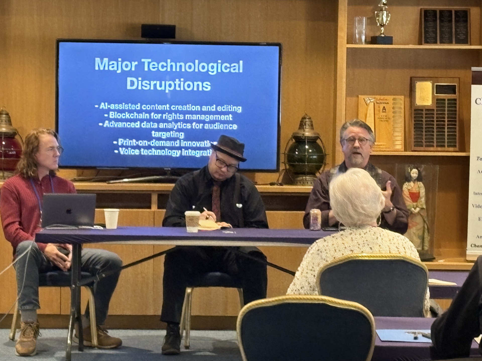 Panel discussion, screen, three men, hat
