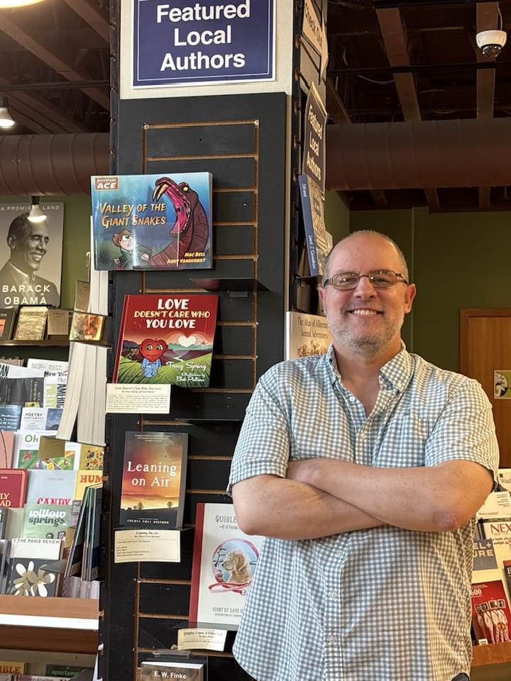 Author standing proudly next to the Featured Author Shelf at Village Books in Bellingham, WA 